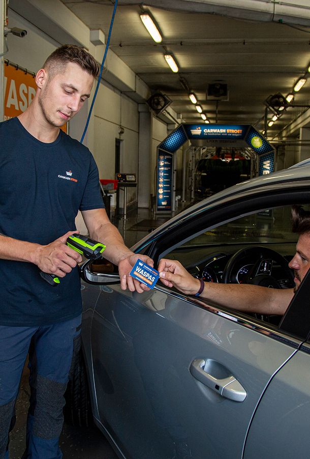 Een man scant een waspas die wordt aangehouden door een automobilist bij een wasstraat.