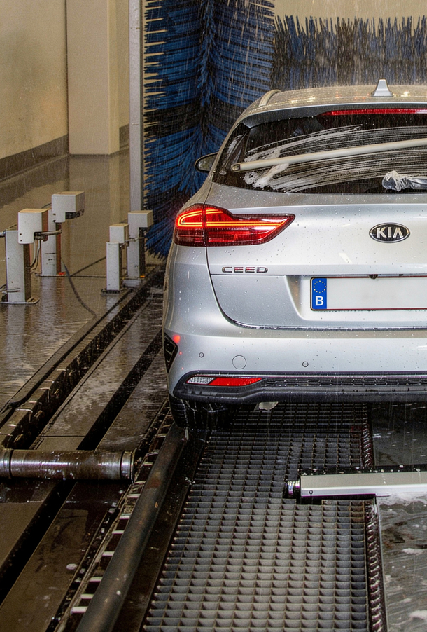 Een zilverkleurige auto wordt gewassen in een automatische autowasstraat met rollende borstels.