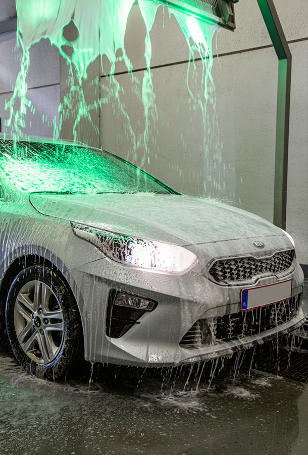 Een witte auto met groene verlichting wordt in een wasstraat gewassen.